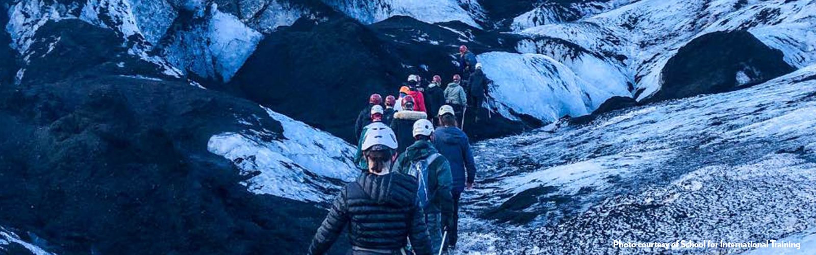 Fifteen students in a line climbing up a narrow section of snowy, rocky mountain. 